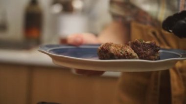 Kırpılmış, elinde maşayla tanınmayan biri lezzetli Salisbury bifteklerini seramik tabağa koyuyor.