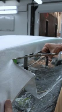 Anonim bir erkek efendinin, atölyede yeni bir sörf tahtası yaratırken fiberglas kumaş parçası kesmek için keskin makas kullanırken elde çekilmiş bir fotoğrafı.