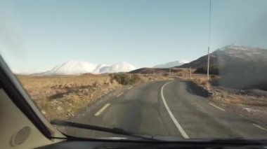 İrlanda 'da dağların arasından geçen yalnız bir araba.