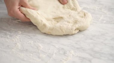 İsimsiz bir kadın mutfakta pizza hazırlarken masaya taze hamur germek için merdane kullanıyor.