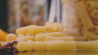 Closeup pan left shot of uncooked macaroni pasta arranged on table with fresh vegetables and leaves prepared for cooking