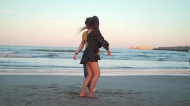 Genç çift dans ediyor ve sahilde günbatımının tadını çıkarıyor. 