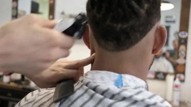 İsimsiz bir kuaförün arkası, yüzü olmayan Afrikalı-Amerikalı bir müşteriye jiletle modern bir saç kesimi yapıyor.