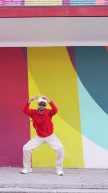 Şehir caddesinde renkli duvarın yanındaki kaldırımda şık giyinmiş, sakallı erkek dansçının statik çekimi.