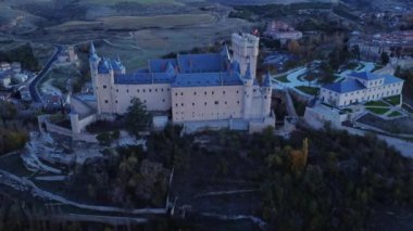 Sonbahar akşamı İspanya 'nın Avila kentinde, yol kenarındaki yemyeşil ağaçların arasında bulunan Segovia' lı Alcazar 'ın insansız hava aracının yukarıdan görünüşü