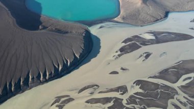 İzlanda 'nın dağlık bölgelerinde kaya oluşumu yakınlarındaki nehir haliçleri ve sakin mavi göl üzerindeki drone manzarasından