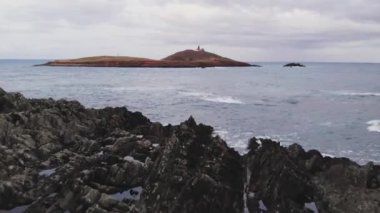 İrlanda 'daki Ballycotton Deniz Feneri Adası' nın önündeki güçlü köpüklü okyanusun üzerinde kayalık uçurumda yürüyen genç kadın yolcuların nefes kesici hava manzarası.