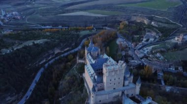 Sonbahar akşamı İspanya 'nın Avila kentinde, yol kenarındaki yemyeşil ağaçların arasında bulunan Segovia' lı Alcazar 'ın insansız hava aracının yukarıdan görünüşü