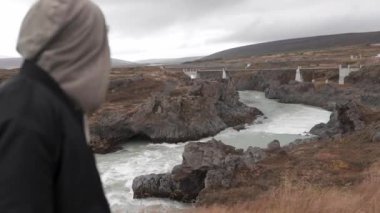 İzlanda 'nın dağlık arazisindeki Skjalfandafljot nehri üzerindeki yaya köprüsünün manzarasını izleyen tanınmamış erkek kaşif.
