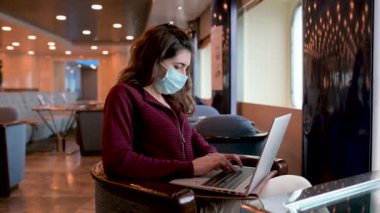 Koruyucu maskeli ciddi bir kadın serbest yolcu gemisinde oturuyor ve netbook 'ta yeni bir proje üzerinde çalışırken daktilo yazıyor.