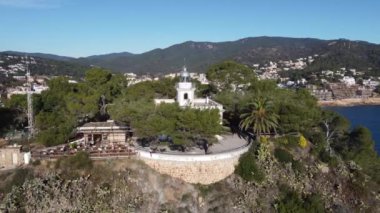 Girona 'da güneşli bir günde muhteşem mavi denize bakan kayalık kayalıklara bakan kulesi olan beyaz kilisenin resimli hava manzarası.