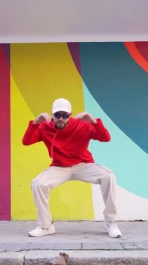 Şehir caddesinde renkli duvarın yanındaki kaldırımda şık giyinmiş, sakallı erkek dansçının statik çekimi.