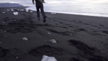 Soğuk mevsimde İzlanda 'da deniz kenarında kumsalda koşup özgürlüğün tadını çıkaran kaygısız erkek maceracı.