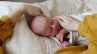 Anne beyaz yatakta uzanan ve sabahları uyuyan sevimli bir bebeği okşuyor.