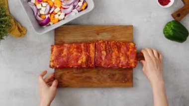 Kırbaçlanmış pirzola ile kesme tahtasını kaldıran ve çiğ havuç ve soğanlı kabağı daha yakın çekerek mutfakta öğle yemeği pişiren ekin sahibinin üst görüntüsü.