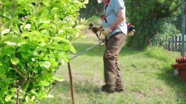 Arka bahçede çim biçme makinesiyle çim biçen yaşlı adam.