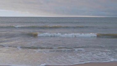 Sakin, sonsuz deniz manzarası köpüklü dalgalar kumlu sahilde süzülüyor ve gün boyunca bulutlu gökyüzüne karşı gelgitler oluyor.