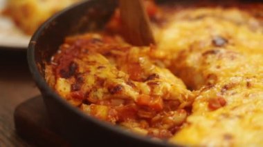 Yüksek açılı, spatula kullanan ve sebzelerle lezzetli graten ve tavada hazırlanmış domates sosu ve peynirle süslenmiş beyaz fasulye servis eden biri.