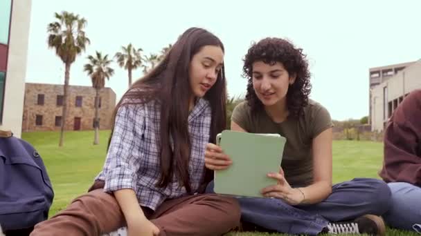 Щасливі Молоді Жінки Повсякденному Одязі Посміхаються Переглядають Планшет Сидячи Траві — стокове відео