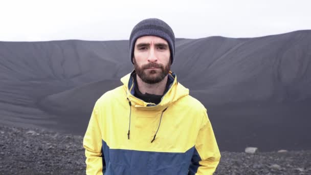 カメラを見ているアイスランドの曇った日の黒いターフ火山の風景を賞賛する外装の男性の旅行者 — ストック動画