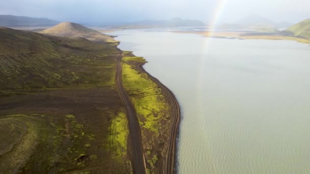 上記の息をのむようなドローンビューから 緑の山とアイスランドの虹と曇った空に対して火山地帯に位置する静かな湖 — ストック動画