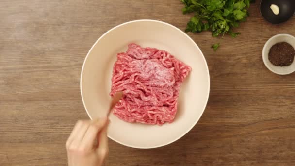 キッチンのテーブルでランチを食べながら 塩と黒唐辛子を新鮮なミンチ肉に加える匿名の人のトップビュー — ストック動画