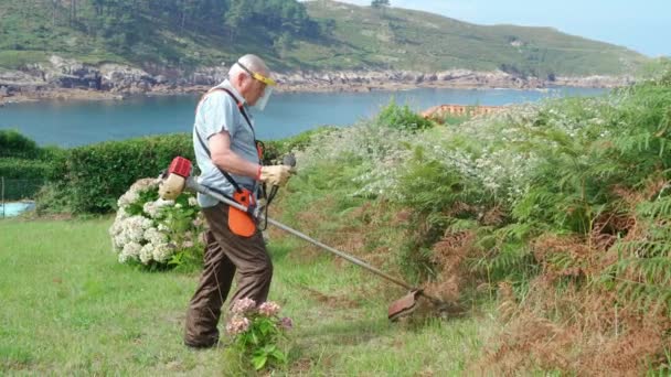 身穿护盾面罩的老人带着割草机在后院割草 — 图库视频影像