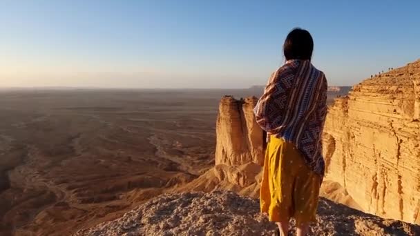 在多风的日子里 穿着黄色衣服的无名女性游客站在陡峭的岩石悬崖边 在无云的天空中欣赏干旱的沙漠 — 图库视频影像