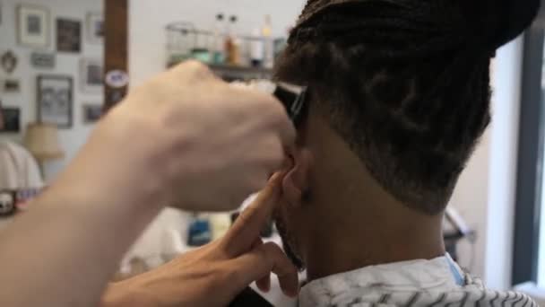 顔のないアフリカ系アメリカ人の顧客に剃刀で現代の散髪を行う匿名の美容師の後ろからのミステリービュー — ストック動画