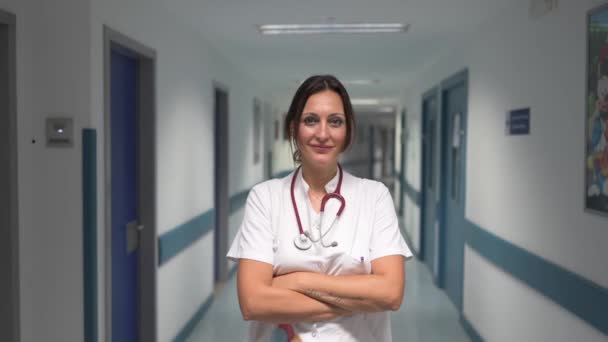 身穿白色制服 头戴听诊器的快乐的女医生站在医院走廊里 看着镜头 — 图库视频影像