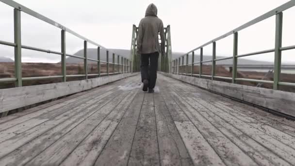 アイスランドの曇った日の金属フェンスとシャビーの古い橋の上に立っている孤独な男性の完全なボディバックビュー — ストック動画