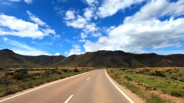 自然公園カボ ナジャール スペインで曇った青空に対して草で山岳地帯を走る空のアスファルト道路を運転 — ストック動画