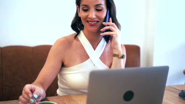 女性起業家がネットブックを使用しながら携帯電話でビジネスプロジェクトを議論し カフェのテーブルでリモートで作業 — ストック動画
