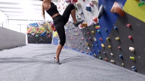 从下面的侧面看穿着运动服和登山鞋的女运动员在攀岩演播室里攀爬墙壁时抓紧抓牢 — 图库视频影像