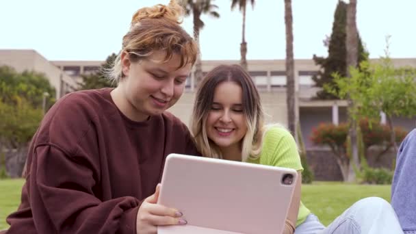 在大学校园里 穿着休闲装的快乐学生坐在草地上笑着用平板电脑 — 图库视频影像