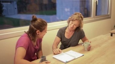 Sıcak bir bardak içecekle tatmin olmuş kadınlar masada oturup notlarda notları tartışıyorlar.