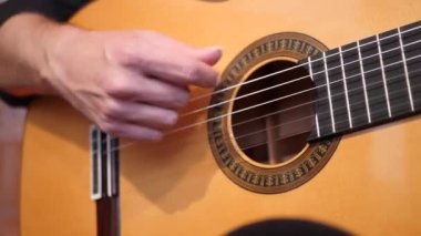 Odada otururken akustik gitarla melodi çalan tanınmamış yetenekli erkek müzisyen.