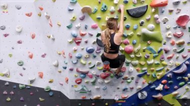Spor giyim sektöründe tanınmayan bir kadın dağcının arka planda parlak saplı kaya duvarına tırmanırken arkadaşının spor salonunda yerde durup rehberlik etmesi.