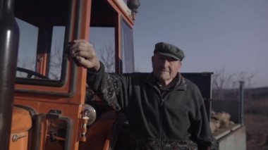 Üst düzey çiftçi traktör kabinine yakın poz veriyor. Çiftlikte kameraya bakıyor.