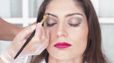 Güzellik salonunda gözleri kapalı oturan çekici bir mankenin yüzüne kaş pigmesi süren isimsiz kadın makyaj sanatçısının arka planı.