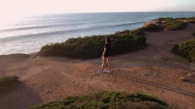 Gün batımında dağlarda spor kıyafetleri içinde koşan genç bir bayan koşucu. Deniz manzaralı. 