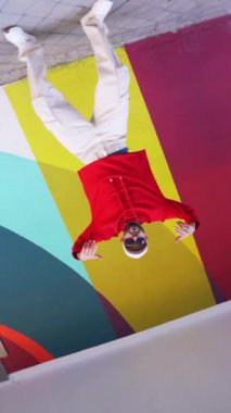 Şehir sokaklarının renkli duvarlarına karşı gösteri sırasında şık giyinmiş sakallı bir adamın kameraya doğru dans edişinin görüntüsü.