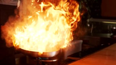 Anonim bir aşçı restoranda yemek pişirirken tavada alevli yemek yapıyor.