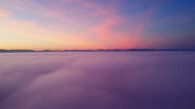 Akşam vakti renkli günbatımında beyaz, kalın ve yumuşak bulutların üzerinde yavaş çekim hava manzarası