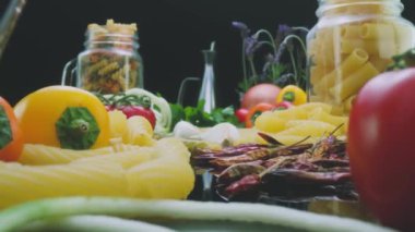 Closeup pan left shot of uncooked macaroni pasta arranged on table with fresh vegetables and leaves prepared for cooking