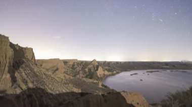 Gece yüzen bulutlar Barrancas de Burujon 'daki sakin göl kıyısındaki kayalık dağ sırtı üzerinde yıldızlı gökyüzü.