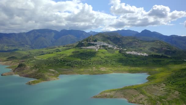 アンダルシア スペイン アンダルシアの曇った青空に対して白い町と緑の山の近くに位置する落ち着いた貯水池の写真のドローンビュー — ストック動画