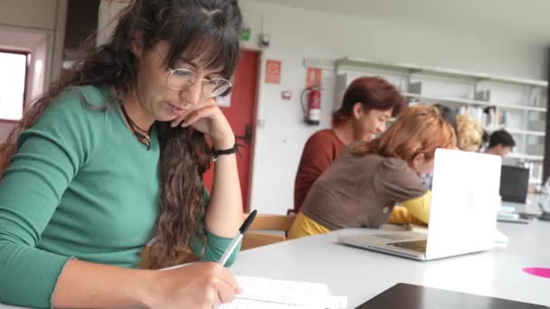 在一所大学的图书馆里 那些穿着休闲装 坐在桌旁为一项研究工作的多愁善感的年轻女性正在和一群其他女性一起学习 — 图库视频影像