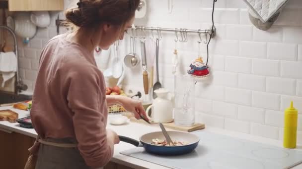 キッチンでの夕食の準備中にパンのスパチュラフライとカットキノコと玉ねぎをかき混ぜる女性 — ストック動画