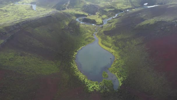 アイスランドの曇りの日の緑の山岳地帯に位置する火山湖や川のドローンビューから — ストック動画